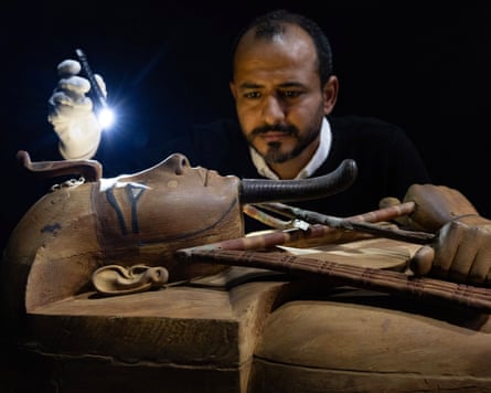 A person holding a flashlight over a wooden coffin