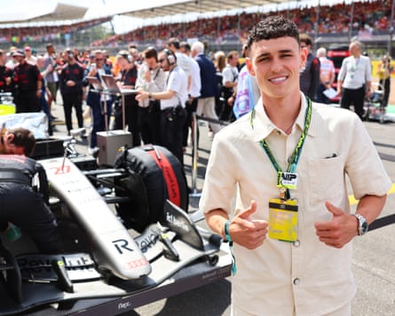 The Manchester City player Phil Foden smiles and gives two thumbs up for the camera while posing in front of the Audi Formula 1 car on the grid at the British Grand Prix at Silverstone.