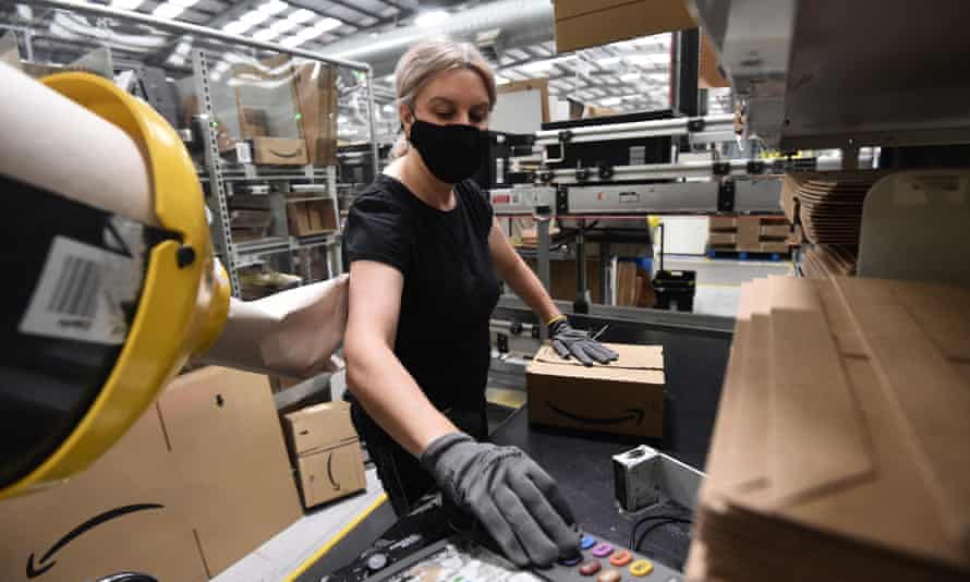 A woman operating the control panel of some machinery in the middle of a busy Amazon warehouse