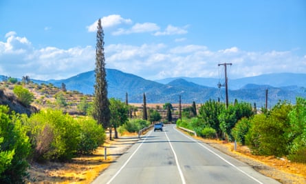 Landscape of Cyprus with cars vehicles riding asphalt road in valley with yellow dry fields, cypress trees and roadside poles, 