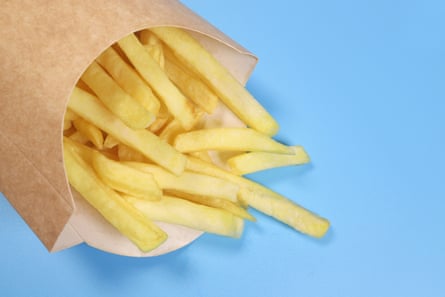 French fries in a brown cardboard fast food carton, being shaken out on to a blue table