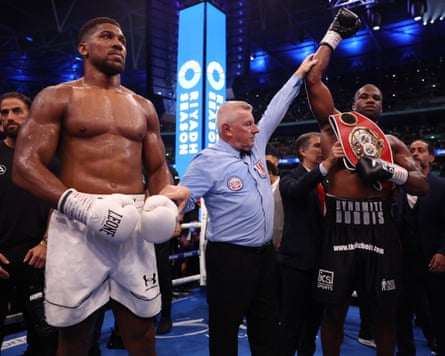 Anthony Joshua (left) stands looking upset as the referee (centre) raises the arm of Daniel Dubois (right) after Dubois won their world heavyweight title fight.