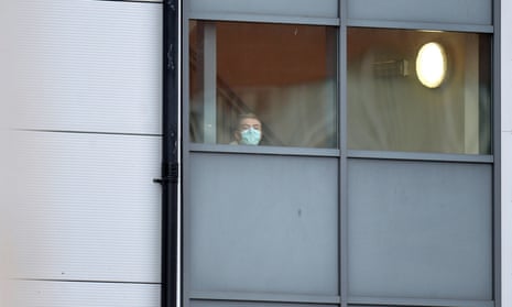 A person wearing a face mask looks out from a window of the accommodation block at Arrowe Park hospital in Wirral.