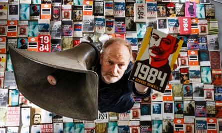 A man holds a wide-mouthed loudspeaker and stands on hundreds of books