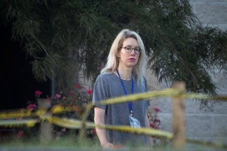 Elizabeth Holmes walks past yellow caution tape near trees at a prison camp