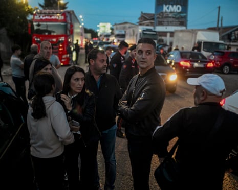 Protesters stand talking on a road crowded with trucks and cars during a blockade at dusk