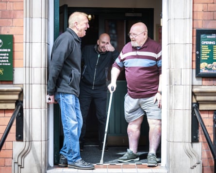 Two men standing in the doorway of a pub, while another behind gives a thumbs up.
