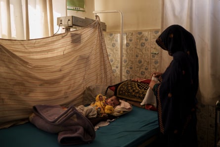 A woman in black dress tends to a newborn baby on a bed in a rudimentary hospital
