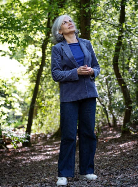 Woman in blue corduroy jacket and dark blue jeans standing in a wood and looking up at the trees
