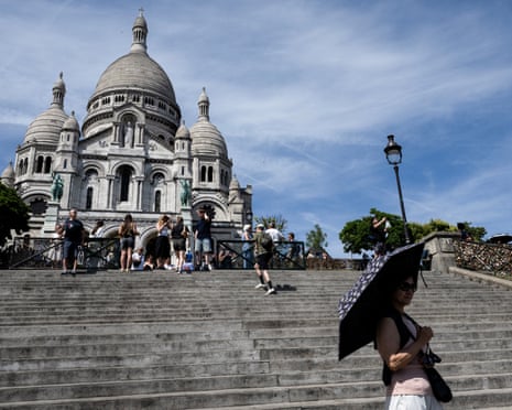 A tourist holds an umbrella as she poses in front of the Sacré-Cœur Basilica during a heatwave in Paris.