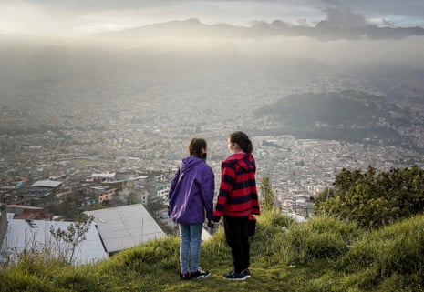 Two girls hold hands on a hill overlooking the city of Quito