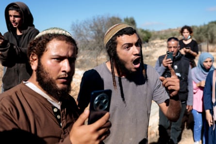 An Israeli settler gestures during an argument as a man next to him holds up a mobile phone, possibly filming