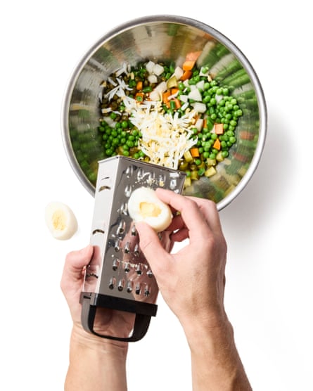 Hands grating the hardboiled eggs into a bowl of chopped vegetables