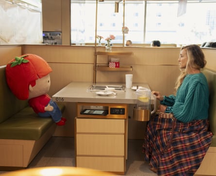 A large stuffed toy of a boy sits across from Carrie in a dining booth