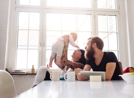 Young tattooed mother and bearded father with newborn baby sitting in their kitchen and having fun together