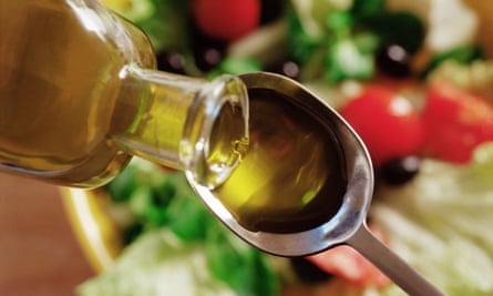 Olive oil being poured on to a spoon with salad blurred in the background