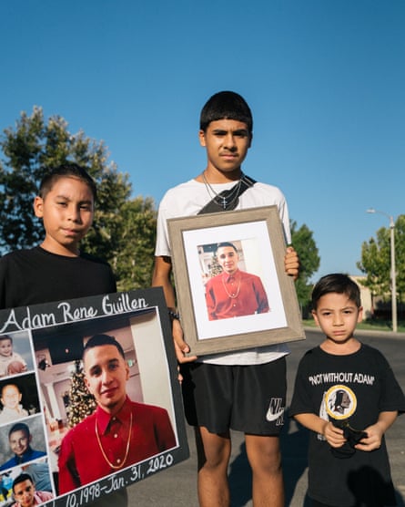 two boys hold up photos while a younger boy wears a T-shirt that says ‘not without Adam’