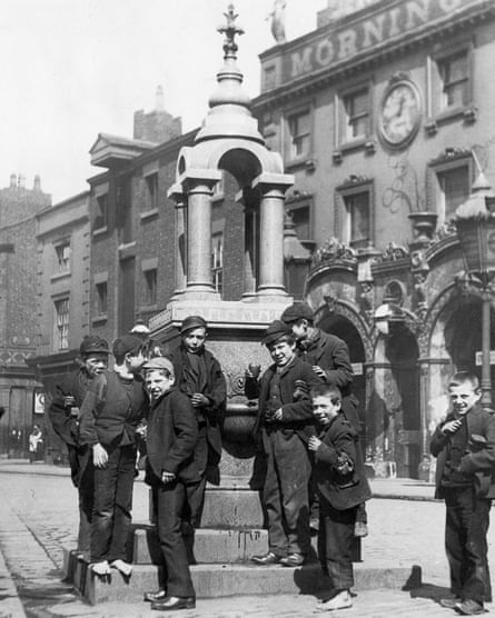 A group of boys gathered for a photograph round a small but ornate drinking fountain, some of them holding up cups of water