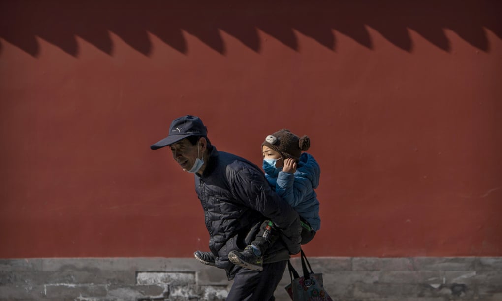 An elderly man carries a young boy on his back as he walks in a public park in Beijing