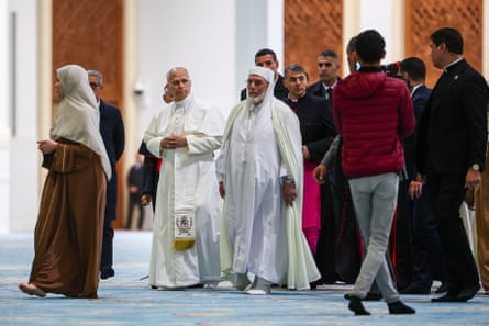 Pope Leo walks alongside Mohammed al-Mamoun al-Qasimi al-Hassani in the Great Mosque of Algiers, as a group of people follow them