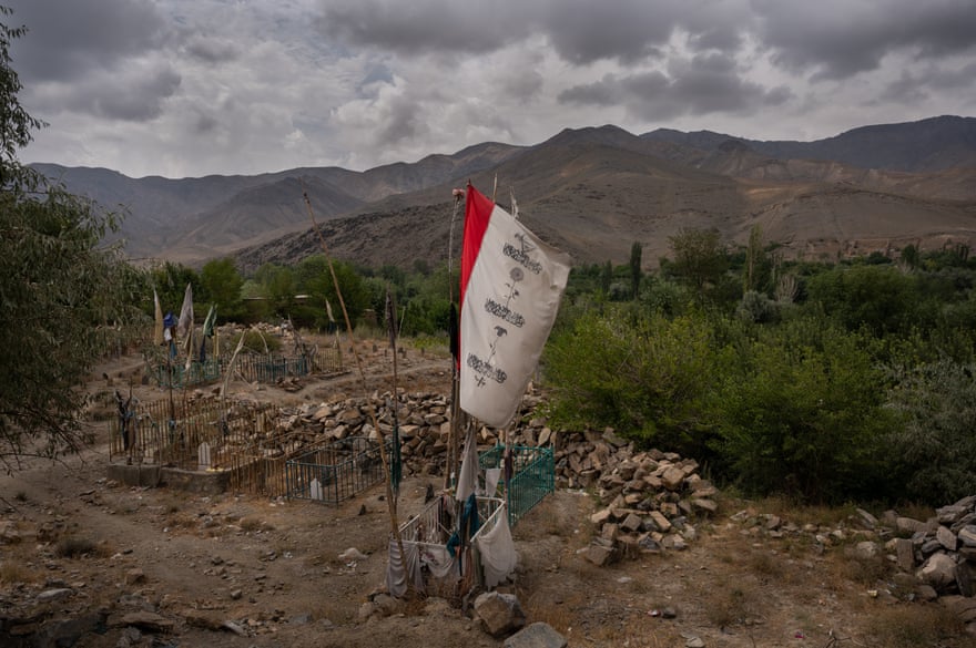A flag painted with a rose, a tulip and a drone releasing bombs flutters flutters over a small cluster of graves in the village of Ismail Khel.