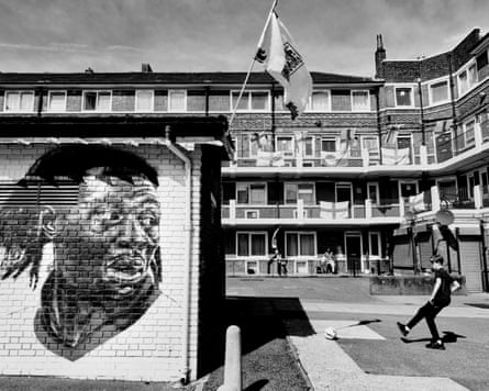 A three-storey block of flats surrounds a courtyard. England flags are hanging over the railings and a mural is painted on a brick wall