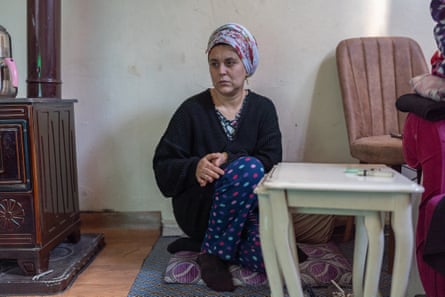 Fatma, wearing a headscarf, sits on the floor with her back against the wall