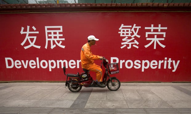 A maintenance worker in China in front of a sign saying Development and Prosperity.