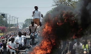 Protesters stand on a car by a fire as they take part in a demonstration in Kisumu