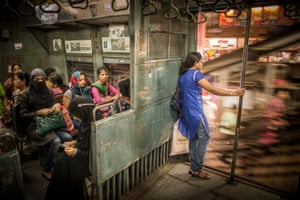 A woman stands at the doorway of a commuter train. The seats are all occupied in this women's compartment of a suburban train in Mumbai, India