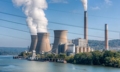 chimneys puffing out smoke at a power plant on the banks of a river