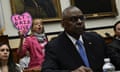A protester behind Lloyd Austin at the hearing holding a 'Let Gaza Live' sign