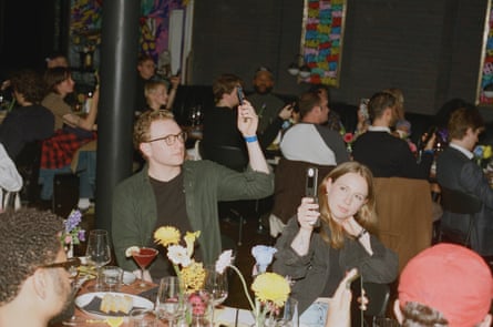 People hold up flip phones while seated for a dinner party