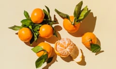 Mandarins, peeled and whole, with stems and leaves attached, on a well-lit light yellow background