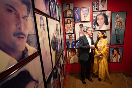 A man and a woman laugh together in front of a gallery wall of photographs of Bollywood actors
