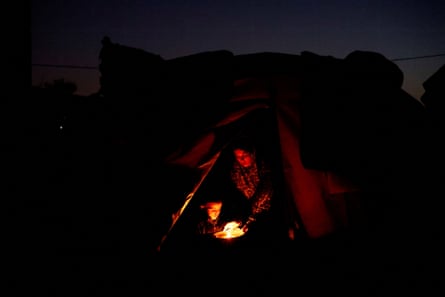 A woman and a child huddle round a small light, possibly a candle, in the dark. The vague outline of a tent entrance can be seen around them