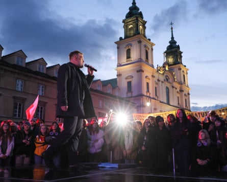 Adrian Zandberg speaks into a microphone on stage as a crowd looks on