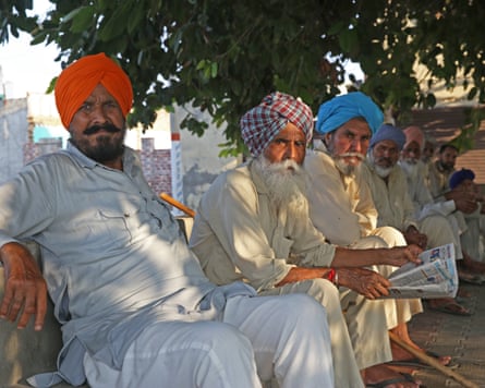 Sikh men in turbans sit in a row in Punjab, one reading a newspaper