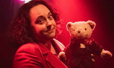 A woman holding a teddy bear in red spotlight.