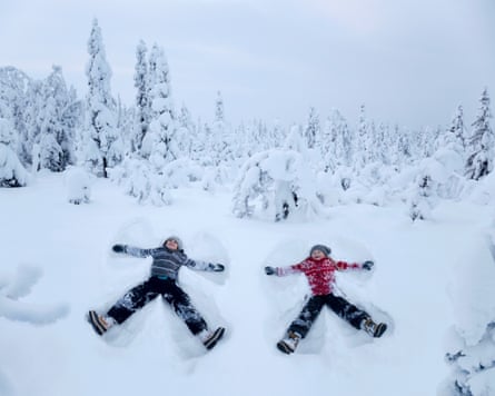 Two children making snow angels in the forest.
