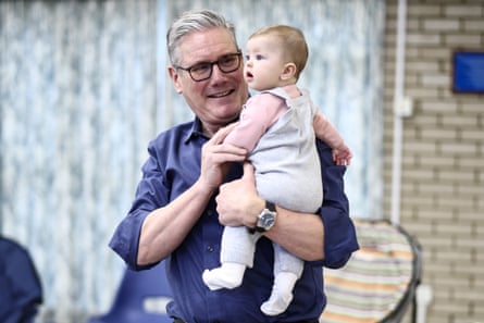Keir Starmer holdsa five-month-old girl during a visit to a “family hub”