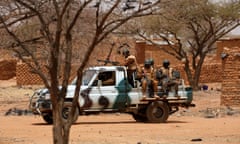 A group of soldiers with weapons sit on the back of a pickup truck