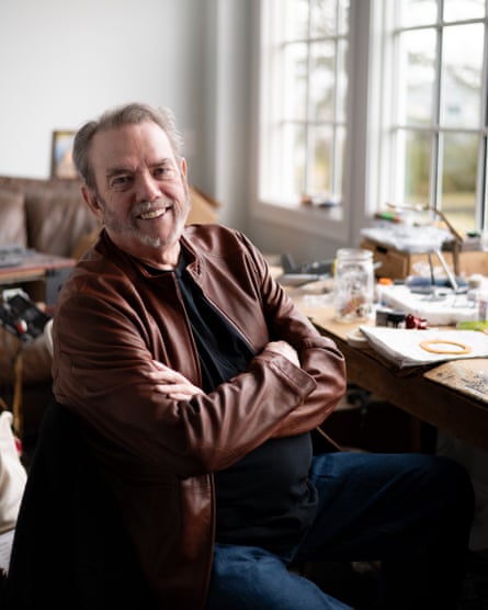 Jimmy Webb wears a brown leather jacket and smiles with his arms crossed as he sits in his home.