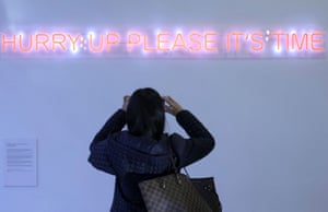 A Cop26 delegate takes a picture of a neon sign, which reads: 'Hurry up please. It's Time.'