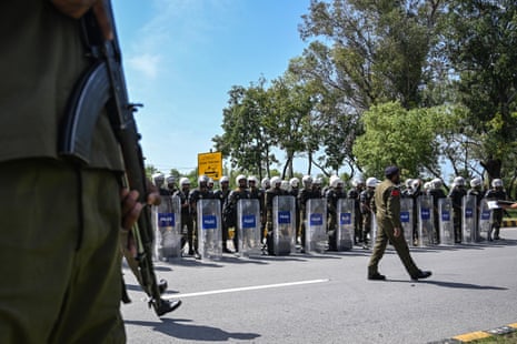 दंगा गियर में दो दर्जन से अधिक पुलिसकर्मी एक पंक्ति में खड़े हैं।