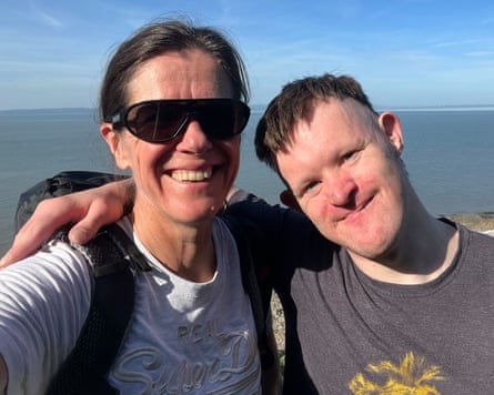 A selfie of a smiling woman wearing sunglasses and a smiling young man with the sea in the background