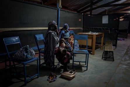 Two mothers sit with their small children on their laps in a dimly lit shed