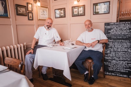 Henry Harris and Dave Strauss sit at a table at Bouchon Racine next to a chalk board showing the day’s menu.