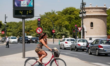 A cyclist waits to cross a road next to a thermometer showing 41C in Valencia, eastern Spain.