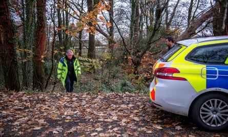 A police officer walks towards her patrol car by a woodland